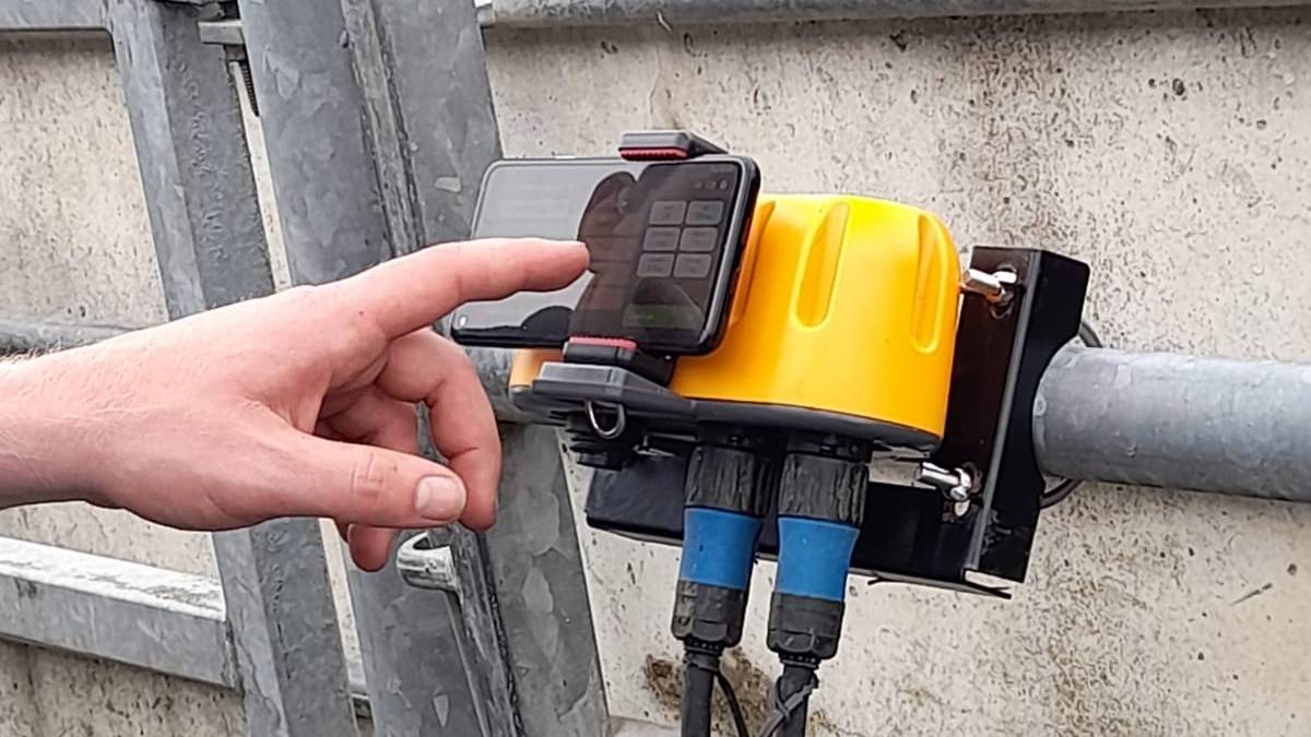 The yellow WeighRite Smart Port clamped to a rail, a phone docked beside it and the load-bar leads below